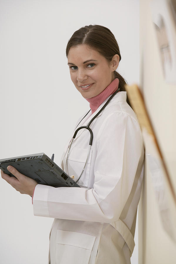 Doctor standing in hallway with laptop computer Photograph by Comstock Images