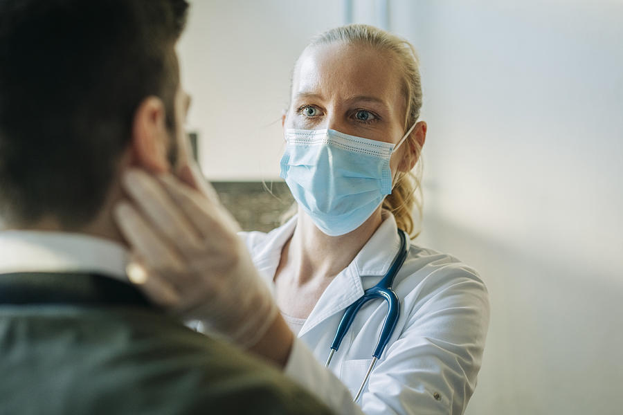 Doctor wearing surgical mask examining man Photograph by Portra