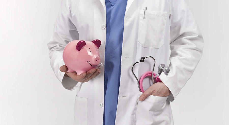 Doctor with piggy bank Photograph by Peter Dazeley