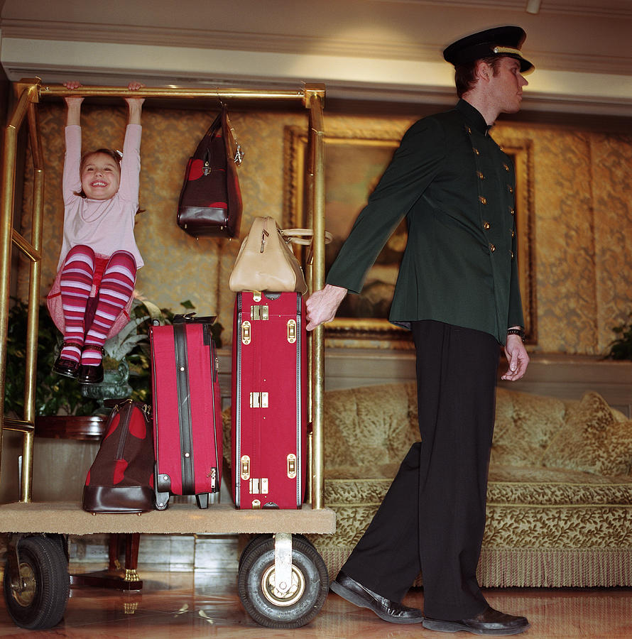 Doorman pulling luggage cart in lobby, girl (4-6) playing on cart Photograph by Tony Anderson Doorman pulling luggage cart in lobby, girl (4-6) playing on cart Photograph by Tony Anderson
