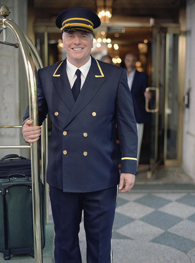 Doorman standing next to luggage cart Photograph by DreamPictures