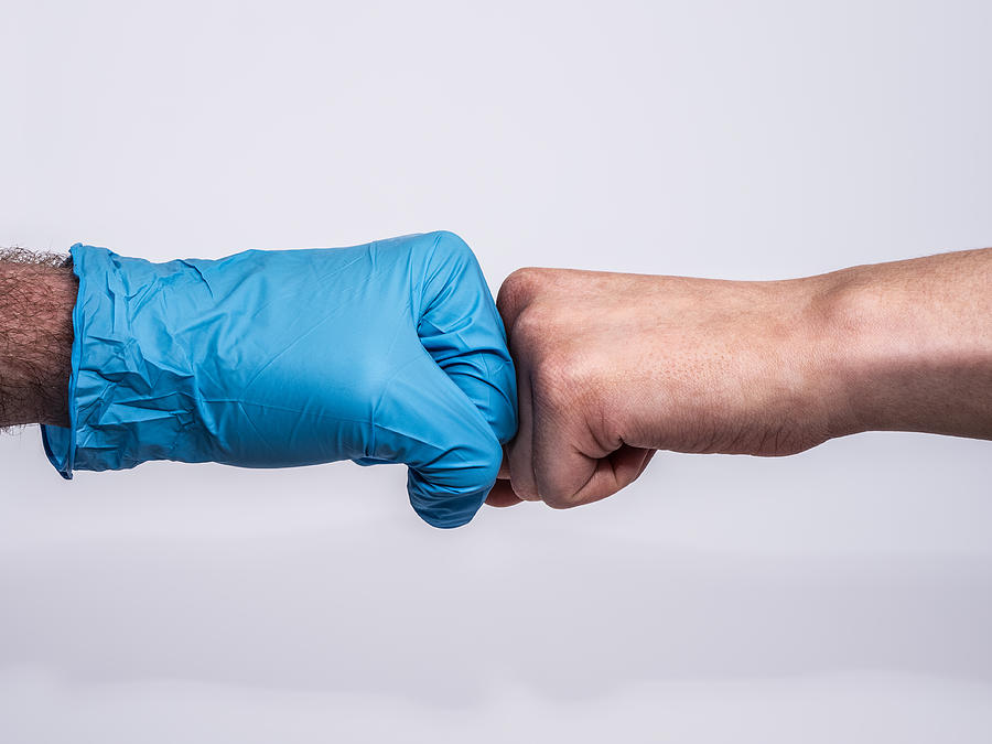 Dramatic handshake with a blue medical glove and a bruised and dirty womans hand, profile view on white background. Photograph by Chris Curry