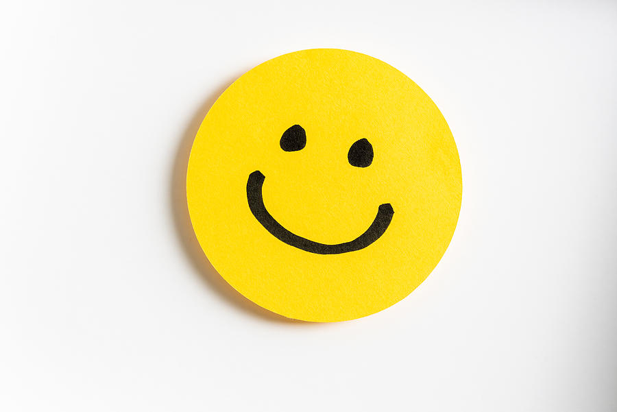 Drawing of a happy smiling emoticon on a yellow paper and white background. Photograph by Zakokor