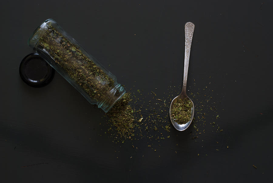 Dried basil on metal teaspoon on dark wooden table Photograph by MichalDziedziak