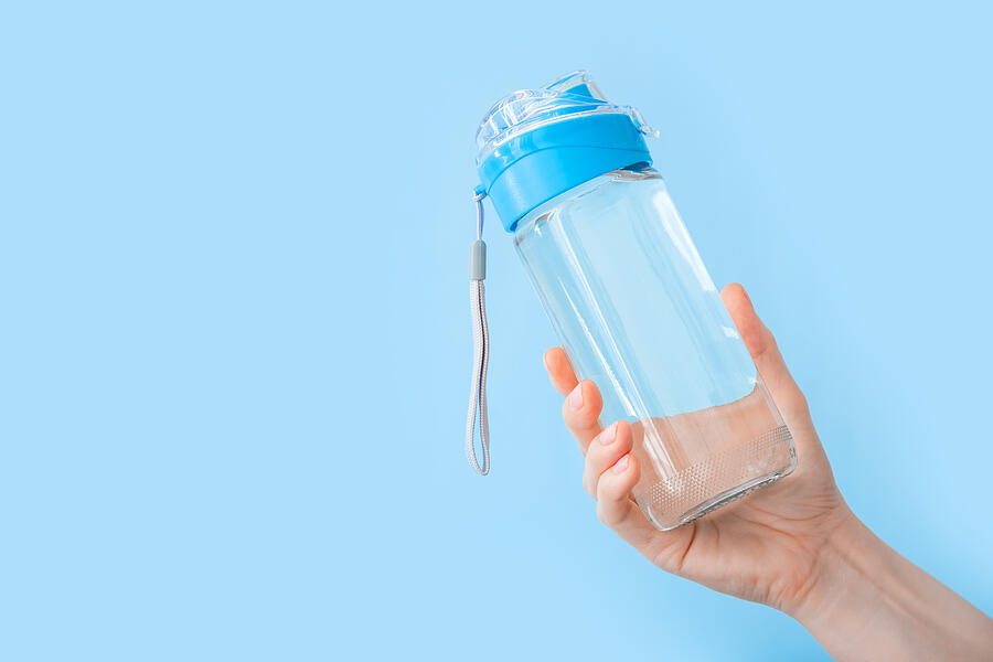 Drinking water bottle for sports in female hand on blue backgraund with copy space. Reusable bottle. Healthy lifestyle and fitness concept Photograph by Beton studio