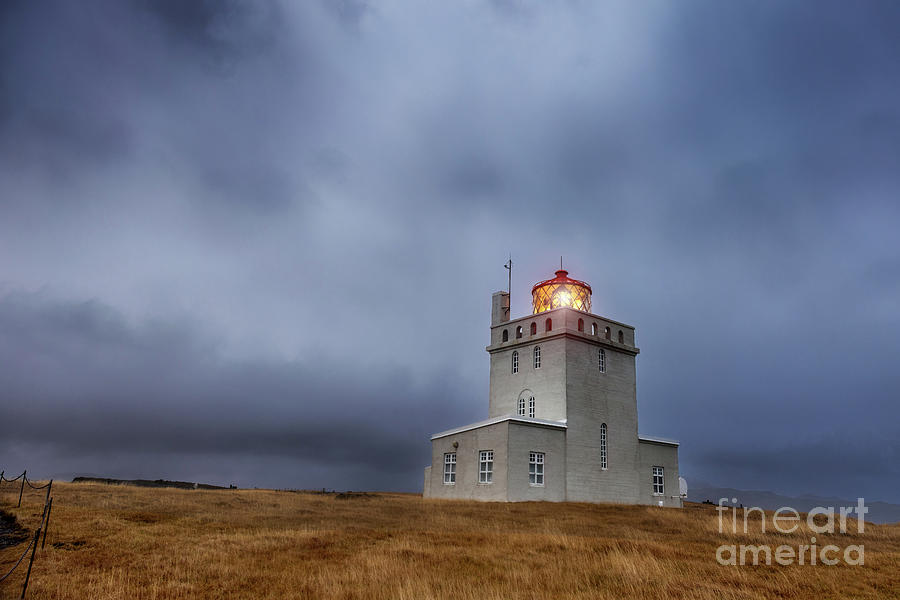 Dyrholaey Lighthouse at blue hour in autumn, the most southerly point on mainland Iceland. Storm clouds are rolling in around the mountains behind Photograph by Jane Rix