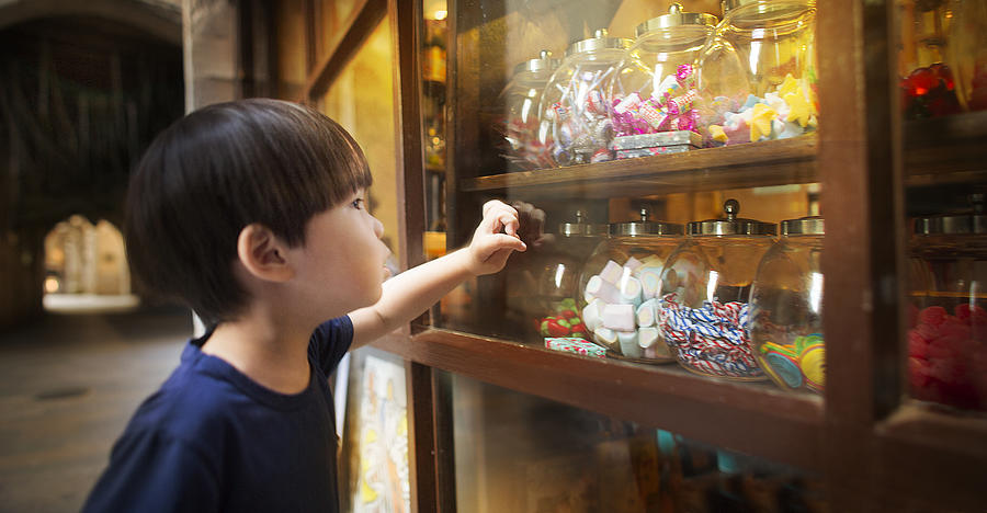 East asian young boy looking at colourful candy jars. Photograph by Twomeows