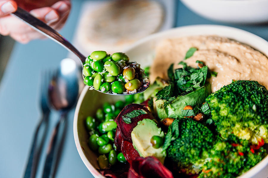 Eating vegan bowl with edamame beans, broccoli, avocado, beetroot, hummus and nuts Photograph by Alexander Spatari