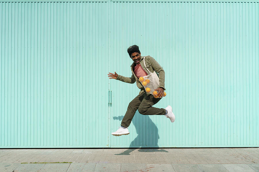 Ecstatic man dancing in front of turquoise wall during sunny day Photograph by Westend61