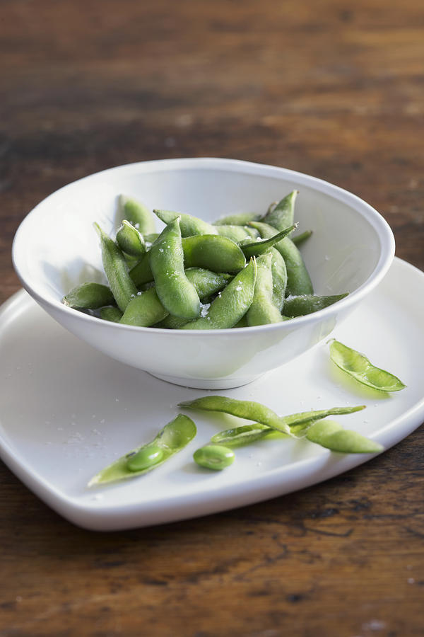 Edamame with salt in bowl on wood table Photograph by Maren Caruso