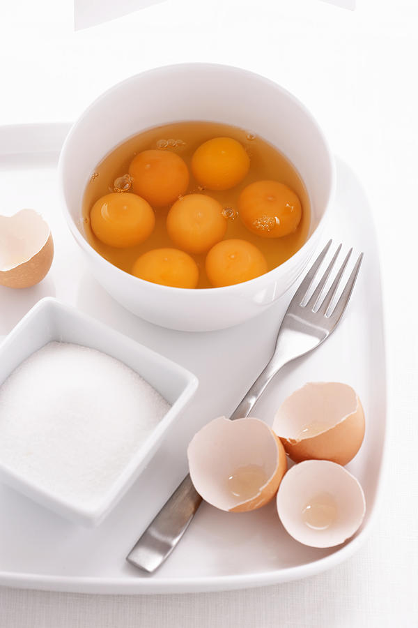 Egg yolks and egg whites in bowl, with eggshells, fork and sugar bowl on tray, close-up Photograph by Martin Poole