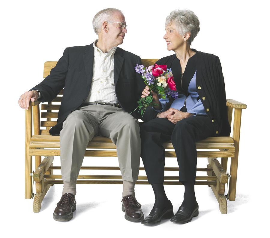 Elderly couple sit on a bench and gaze lovingly into each others eyes. Photograph by Photodisc