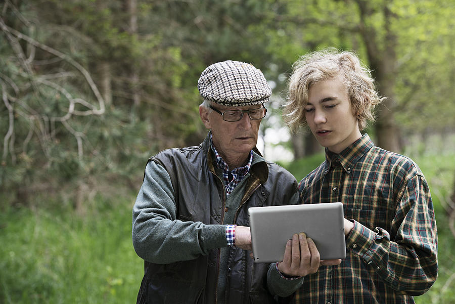 Elderly man and boy in forrest looking at tablet computer Photograph by Robin Skjoldborg
