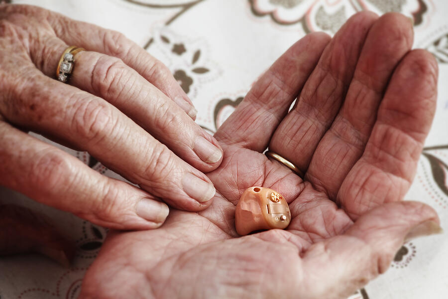 Elderly Womans Hands Holding A Modern Hearing Aid Photograph by Andrew Bret Wallis