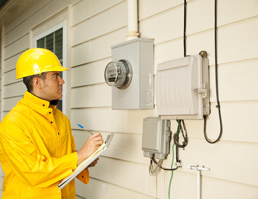 Electrician, repairman at outside electric meter on home. Yellow raincoat. Photograph by Fstop123