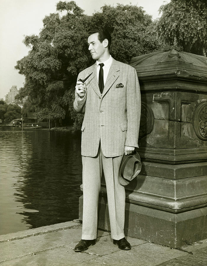 Elegant man smoking pipe by park lake, (B&W), portrait Photograph by George Marks