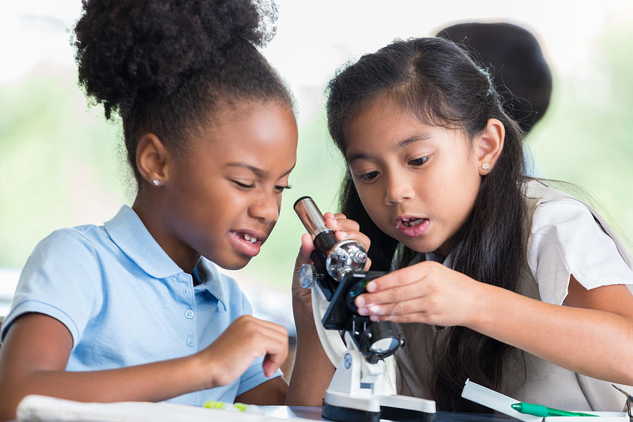 Elementary school friends use microscope in science class Photograph by SDI Productions