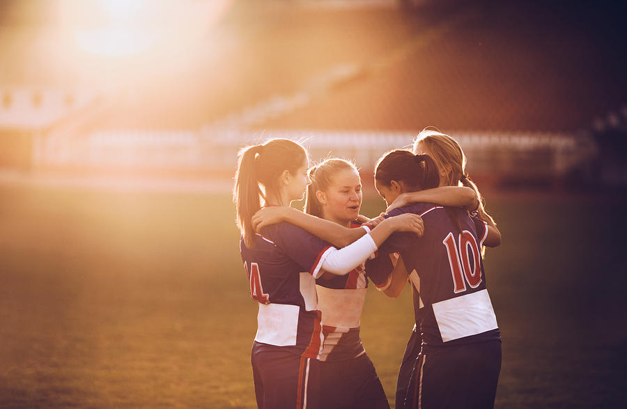 Embraced female soccer players celebrating on a playing field at sunset. Photograph by Skynesher