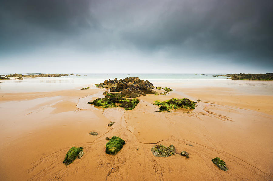 Empty beach with rocks and dark sky Photograph by Philippe Lejeanvre