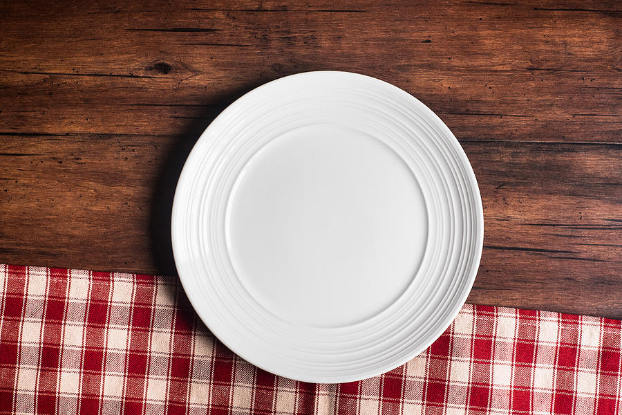 Empty white plate on a napkin on an old wooden brown background, top view. Image with copy space. Kitchen table with a towel and a plate - top view with copy space. Photograph by Anna Kurzaeva