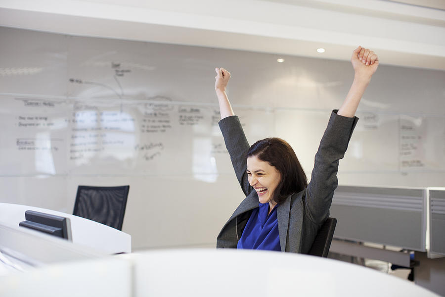 Enthusiastic businesswoman with arms raised in office Photograph by Robert Daly