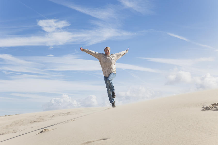 Enthusiastic mature woman running along sand dune Photograph by Westend61