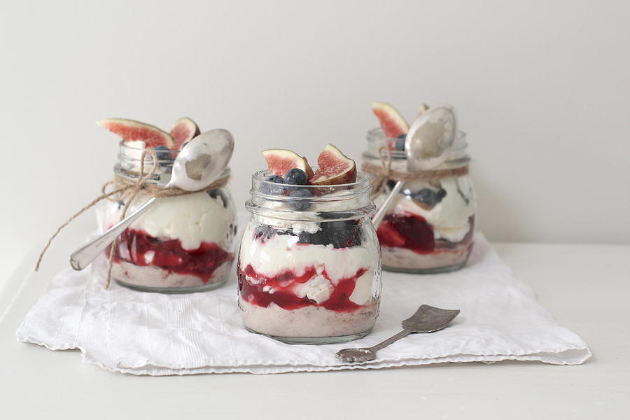 Eton mess desserts in jars topped with fresh figs and blueberries Photograph by Emmaduckworth