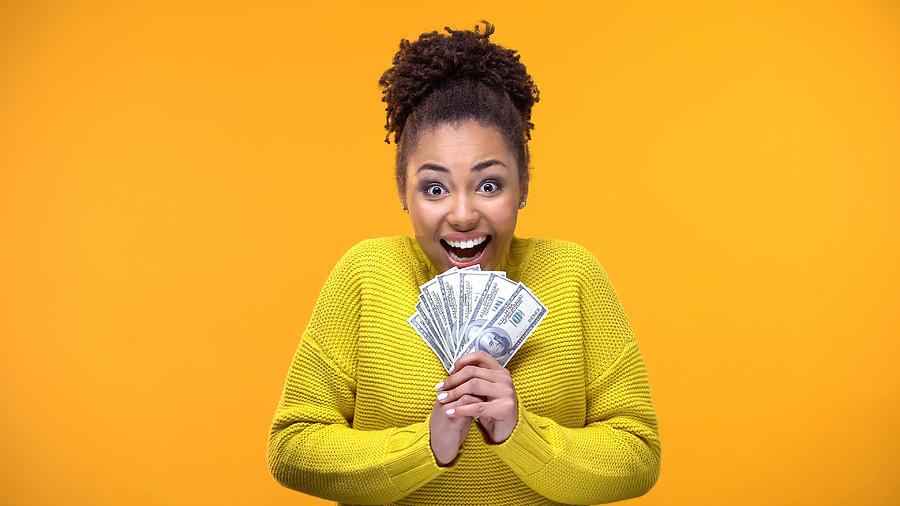 Excited Afro-American woman holding bunch of dollars, lottery winner, fortune Photograph by Motortion