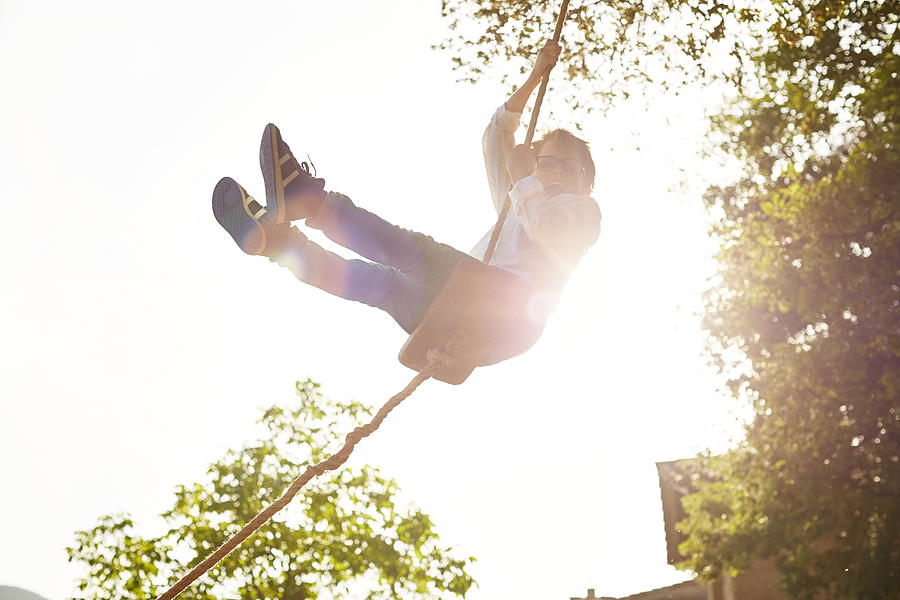 Excited boy swinging at back yard on sunny day Photograph by Morsa Images