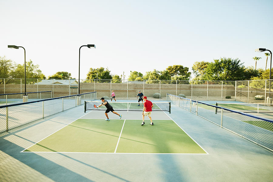 Extreme wide shot of senior friends playing doubles pickleball on sunny summer evening Photograph by Thomas Barwick