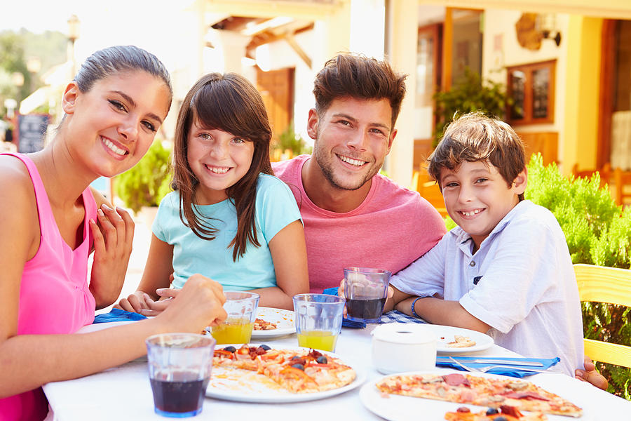 Family eating pizza at outdoor restaurant smiling for camera Photograph by Monkeybusinessimages