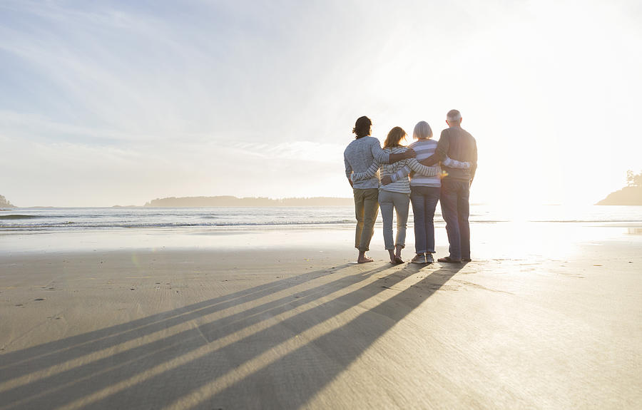 Family hugging on beach looking at ocean view at sunset Photograph by Compassionate Eye Foundation/Steven Errico