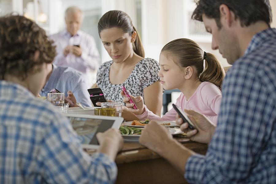 Family including kids (8-9) texting at dinner table Photograph by Hiya Images/Corbis