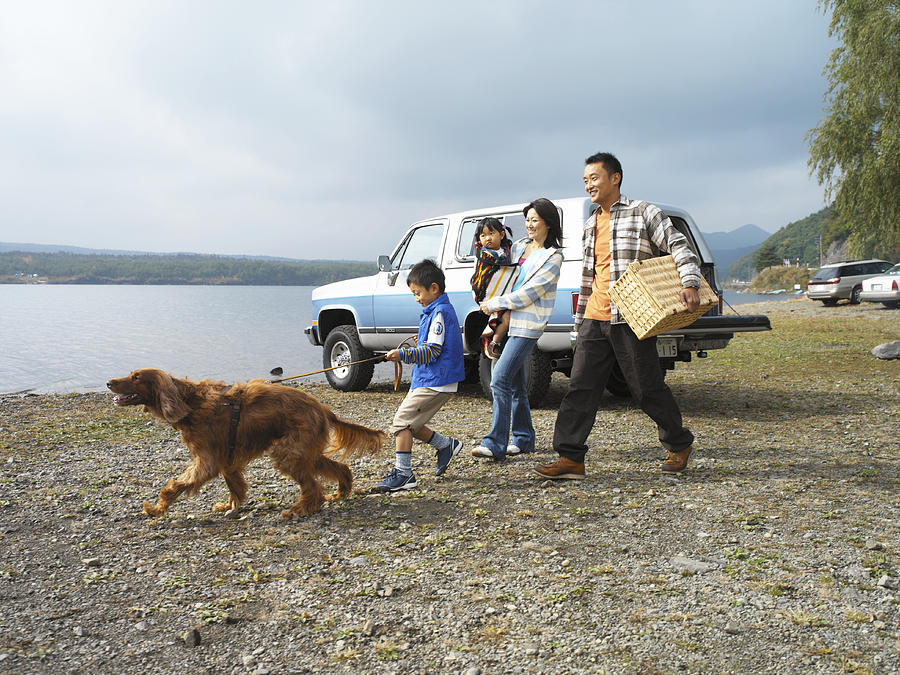 Family of four and dog on shore by car, father carrying hamper Photograph by Kei Uesugi