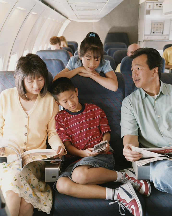 Family of Four Sit on a Plane, Reading Magazines and Playing Computer Games Photograph by Digital Vision.