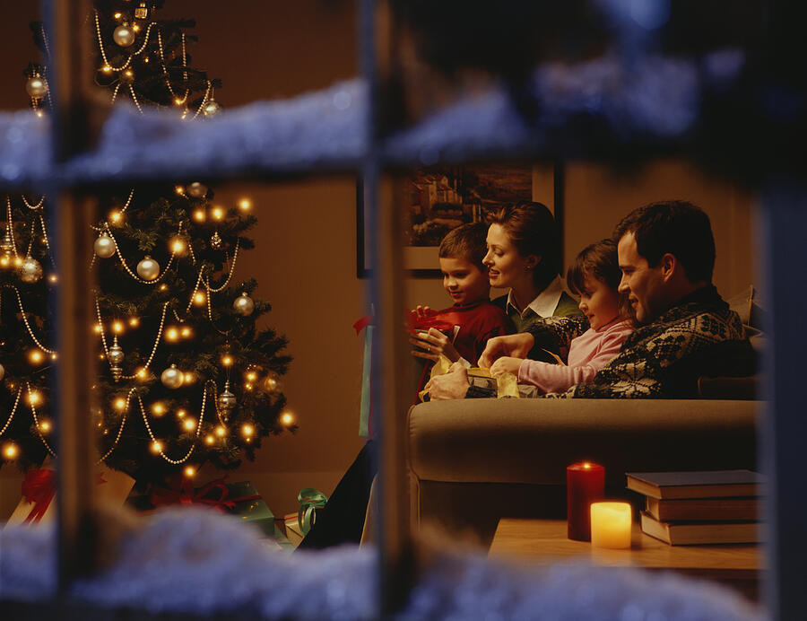 Family opening gifts on Christmas Eve, viewed through window Photograph by Ryan McVay