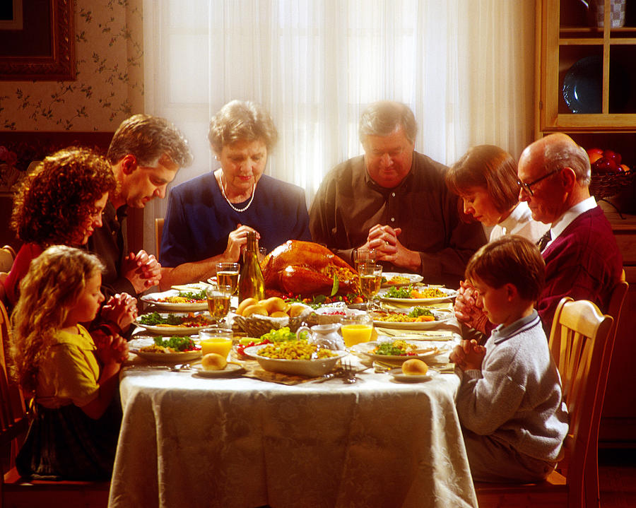 Family praying together over Thanksgiving dinner Photograph by Burke/Triolo Productions