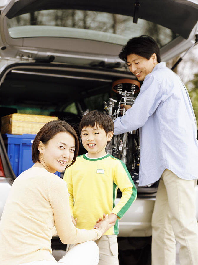 Family Standing by the Back of Car, with the Father Removing a Bicycle Photograph by Digital Vision.