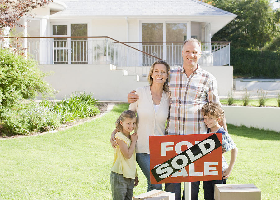 Family standing with sold sign of their new house Photograph by Martin Barraud