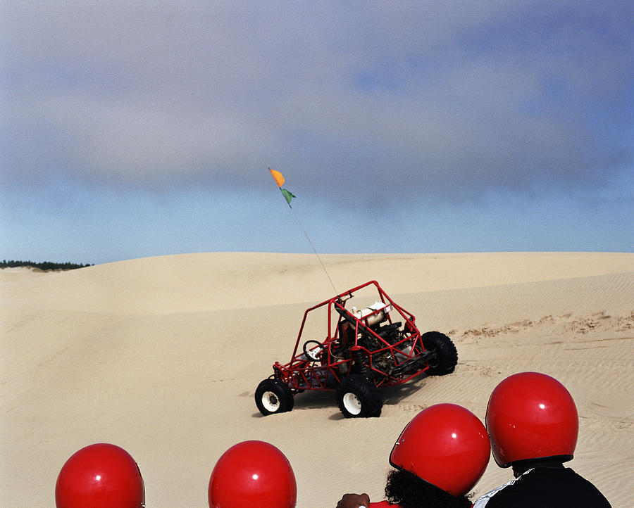 Family wearing crash helmets, looking at dune buggy, rear view Photograph by Ryan McVay
