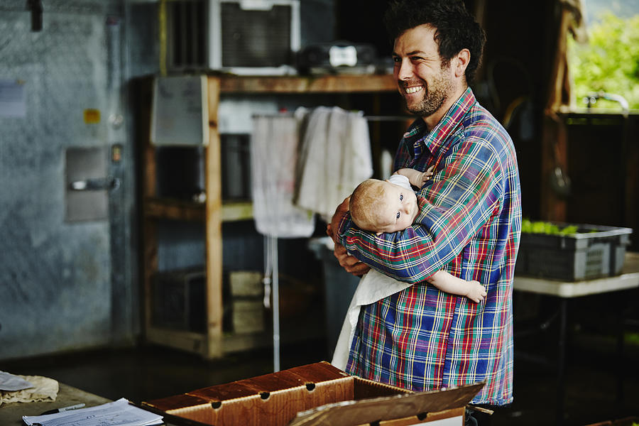Farm owner holding infant daughter in work shed Photograph by Thomas Barwick