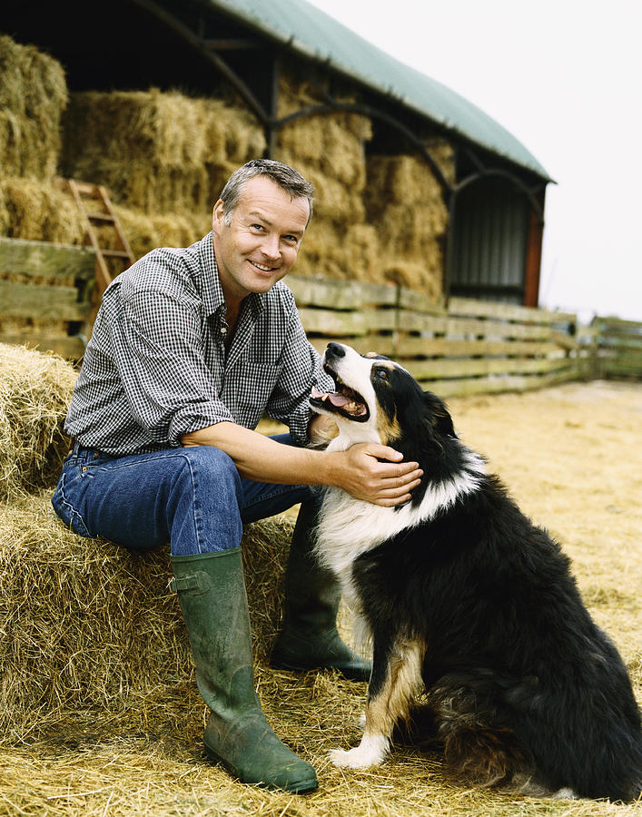 Farmer Sitting on a Bay of Hale on a Farm With His Pet Dog Photograph by Digital Vision.