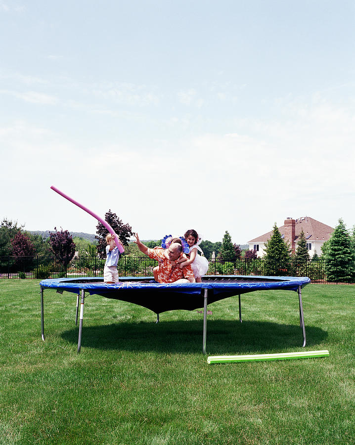 Father and children (2-8) playing on trampoline on lawn Photograph by MoMo Productions
