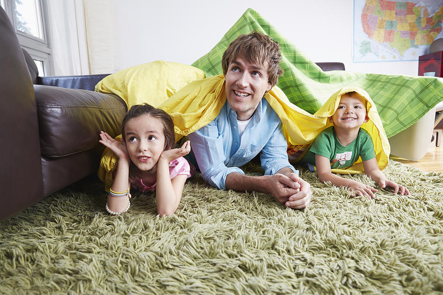 Father and children playing in blanket fort in living room Photograph by Jasper Cole