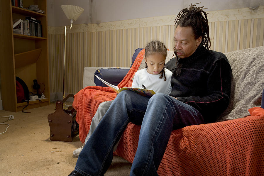 Father and daughter on sofa with book Photograph by Jw Ltd