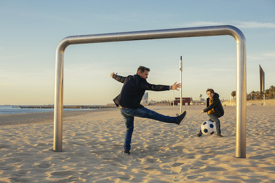Father and son playing football on the beach Photograph by Westend61
