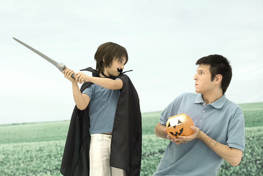 Father and son playing, man holding jack o lantern, boy swinging sword Photograph by PhotoAlto/Odilon Dimier