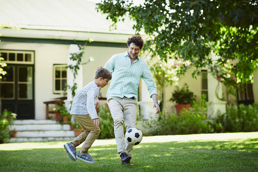 Father and son playing soccer in lawn Photograph by Morsa Images
