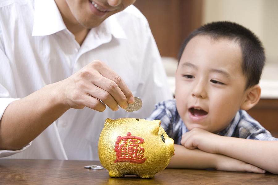 Father and son saving coins into a piggy bank Photograph by Lane Oatey