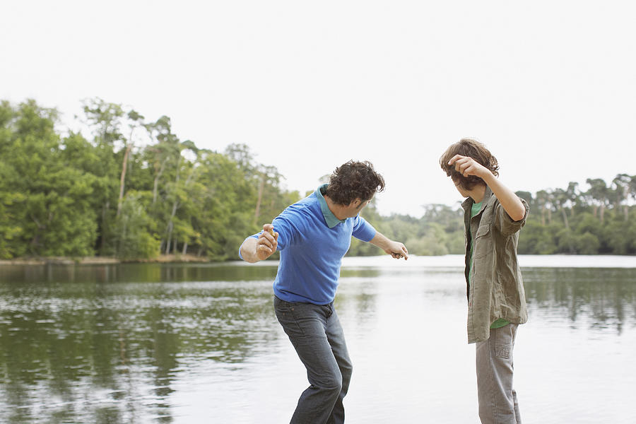 Father and son skimming stones in lake Photograph by Sam Edwards